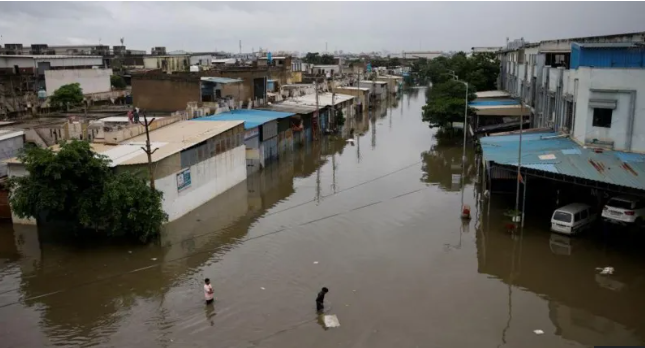 People cross a flooded street after heavy rains in Ahmedabad